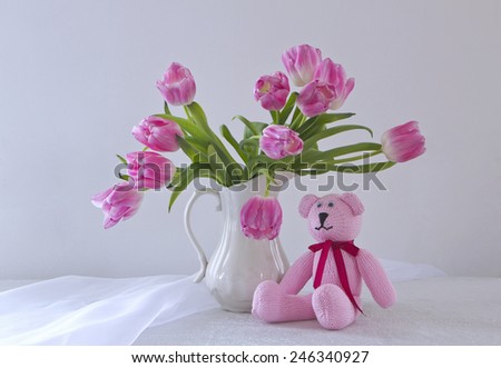 beautiful bouquet of pink tulips in a jug with sitting next to knit a pink teddy bear