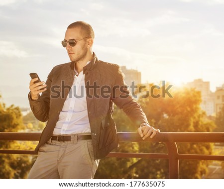 Young man using a smart phone outdoors / focus on face of young man in the photo shop added the sun and the color of the background.