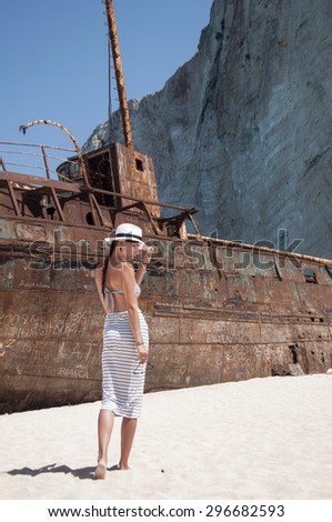 Woman in skirt and a hat on background a ship wreck