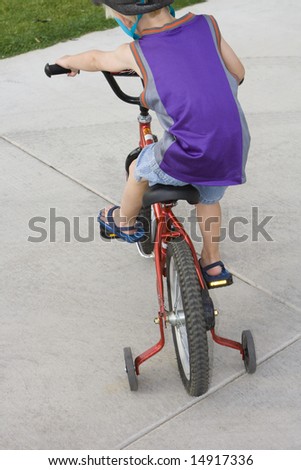 Young boy riding a bike with training wheels on a driveway