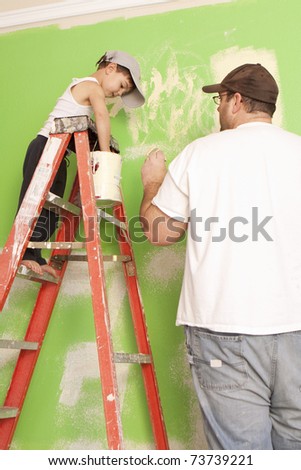 Young boy standing on a ladder helping his dad paint.