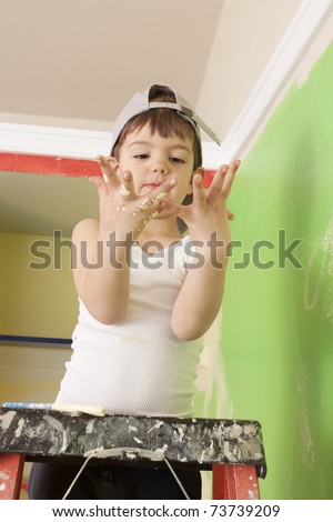 Little boy in painting clothes on ladder looking at his painted hands.