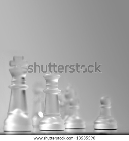 Shallow depth of field view of a chess board centered around the white queen, other pieces in soft focus in smooth gray background. Plenty of copyspace for presentation usage.