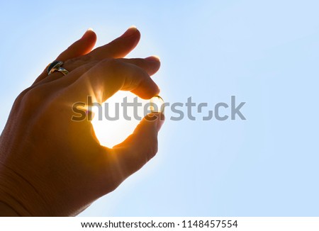 Vitamin D keeps you healthy while lack of sun. Hand holding yellow soft shell fish oil capsule against sun and blue sky on sunny day.