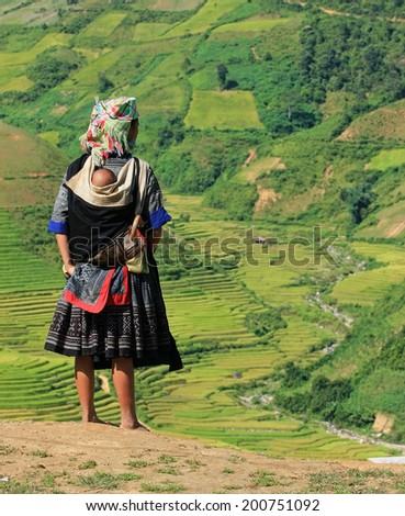 An unidentified Hmong woman standing on the side of a mountain pass and taking a look around a valley of paddy field.