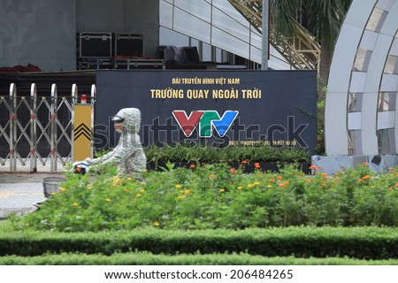 HANOI, VIETNAM - JUL 13, 2014: Unidentified Vietnamese woman riding a motorbike passing the front of Vietnam Television (VTV) station\'s gate. VTV is the officially central state owned media channel.
