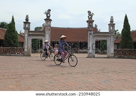 HANOI, VIETNAM - AUG 12, 2014: Unidentified Vietnamese women cycling in front of a temple in Duong Lam ancient village, Hanoi capital, Vietnam.