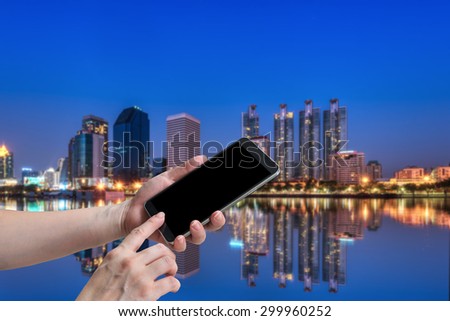 woman hand hold and touch screen smart phone, on business building blurred  background.