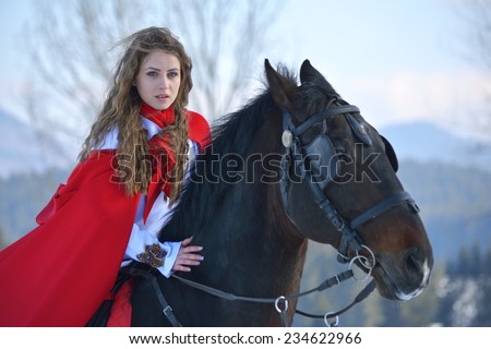 Beautiful blonde woman with red cloak with horse outdoor in winter season