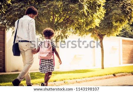 African American father and his daughter walking trough park. From back.