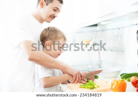 Happy father teaches son to cut vegetables for salad.