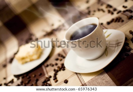 Very hot coffee in cup and cake on table, cake in blurred background