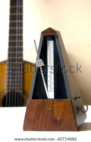 Old metronome over white table with guitar behind (vertical photo)
