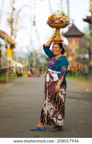 BALI, INDONESIA - JUNE 2: Balinese woman loads the offering of food in wooden jar on her head for the ceremony in Ubud temple, Bali on June 2, 2014