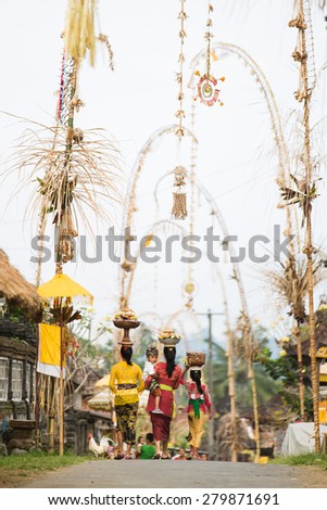 BALI, INDONESIA - JUNE 2: Balinese woman with cild loads the offering of food in wooden jar on her head for the ceremony in Ubud temple, Bali on June 2, 2014