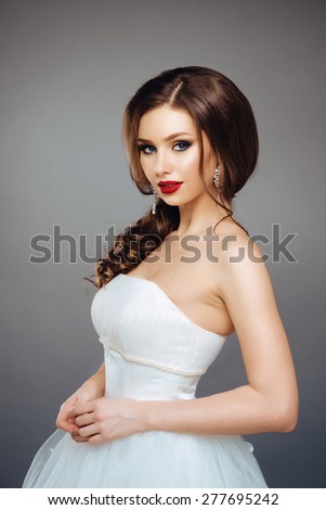 Fashion Studio Portrait of Beautiful Elegance Bride with Dark Hair in Luxurious Wedding White Dress. Fashion MakeUp and Coiffure. Red Lips