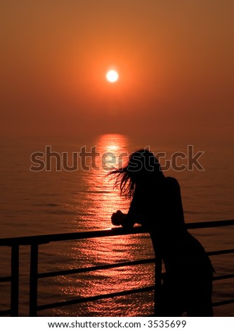 Girl looking at the Sunset over the Ocean, with the hair dancing in the wind