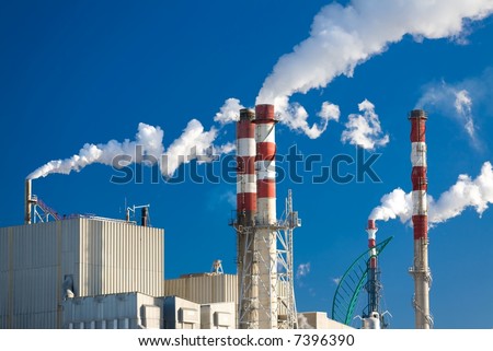 Paper factory with main chimneys expelling smoke into a deep blue sky - horizontal orientation