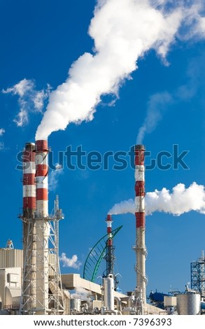 Paper factory with main chimneys expelling smoke into a deep blue sky - vertical orientation