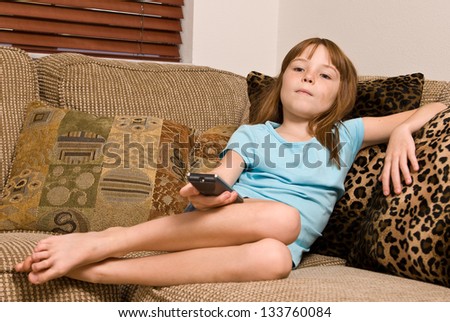 Young female child holding a remote while watching television