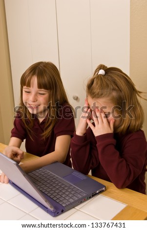 Young girls working on a laptop computer - One young girl covers her face in  as the other girl smiles and points out, what appears to be a mistake, on the screen