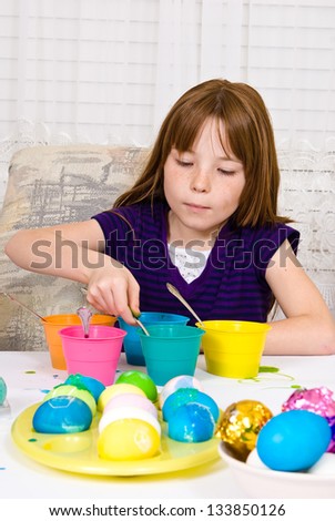 Young girl in the process of coloring Easter Eggs - Step five, the egg completely submerged in the cup of dye