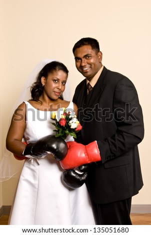 A young ethnic couple wedding attire wearing boxing gloves.