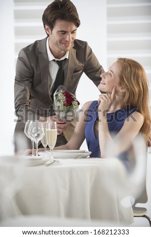 romantic man giving flowers to his girlfriend in a restaurant