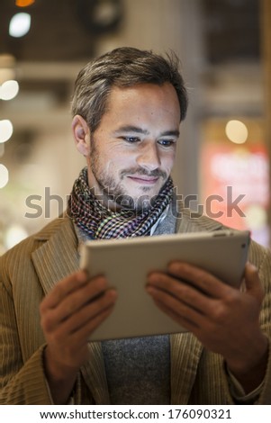 handsome man using a digital tablet outside with city lights at the background