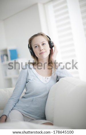 beautiful young woman listening to music with wireless headset sits on her couch