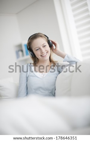 beautiful young woman listening to music with wireless headset sits on her couch