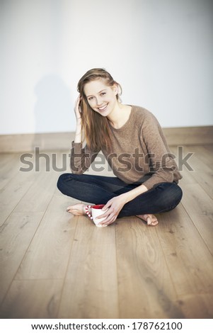 beautiful natural young woman sits on wooden floor with a cup of tea