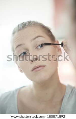 beautiful young woman applying makeup on her eyelashes in front of her mirror
