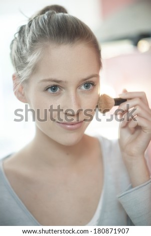 beautiful young woman applying makeup before her mirror