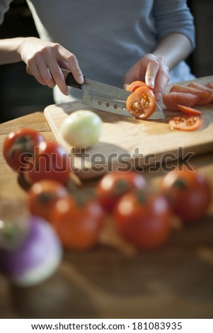 closeup of hands slicing tomatoes on kitchen\'s table tomatoes blurred at foreground