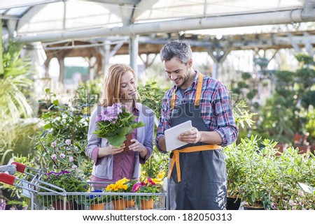 gardener using his digital tablet to advise a female client who buys flowers