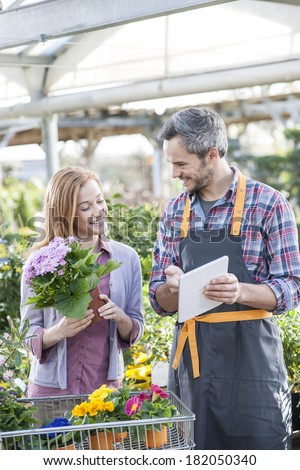 gardener using his digital tablet to advise a female client who buys flowers