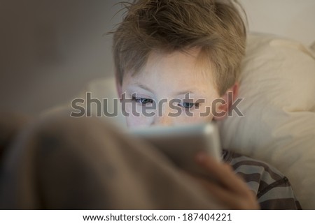 little boy at expressive face using a digital tablet in bed