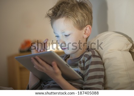 little boy at expressive face using a digital tablet in bed
