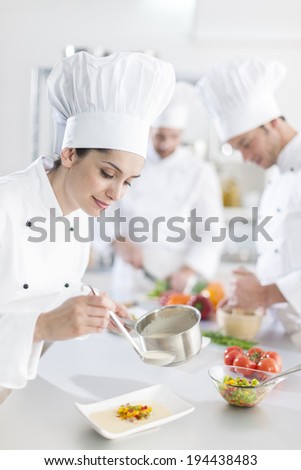 female chef preparing a dish her team in the background