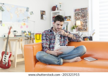 young man sitting on the couch and surfing on a digital tablet