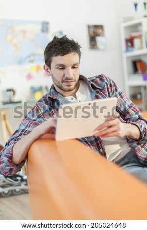 young student lying on a couch surfing  the web  on his digital tablet