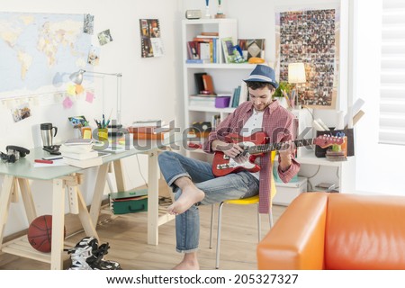 young student is playing guitar in his apartment