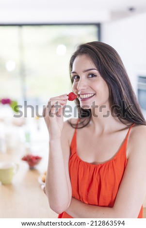 cheerful young woman in the kitchen with a strawberry in hand