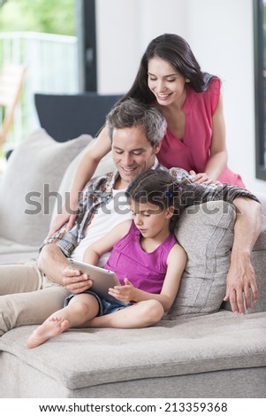 family sitting on a couch looking at a digital tablet