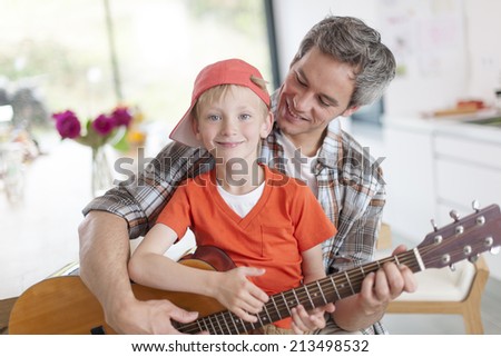 father learning his boy to play guitar