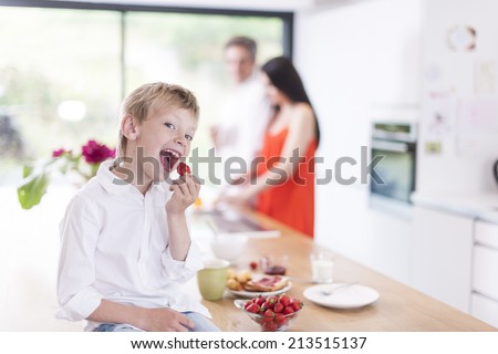 young boy eating  strawberries in family kitchen