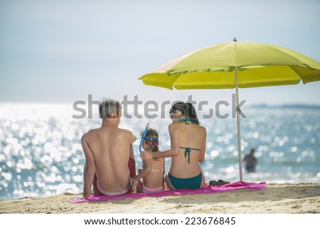 family in swimsuit at the beach sitting under an umbrella watching the sea