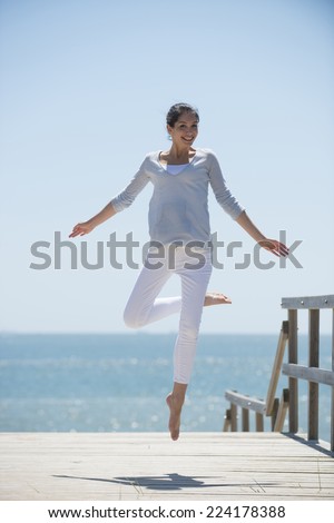 young woman full of energy jumping on a pontoon in front of the sea on a sunny day