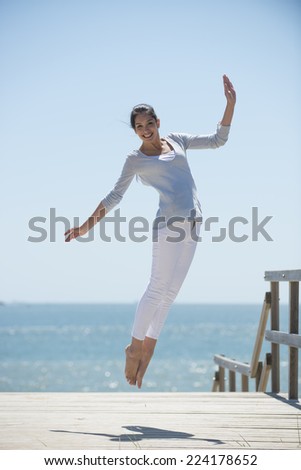 young woman full of energy jumping on a pontoon in front of the sea on a sunny day